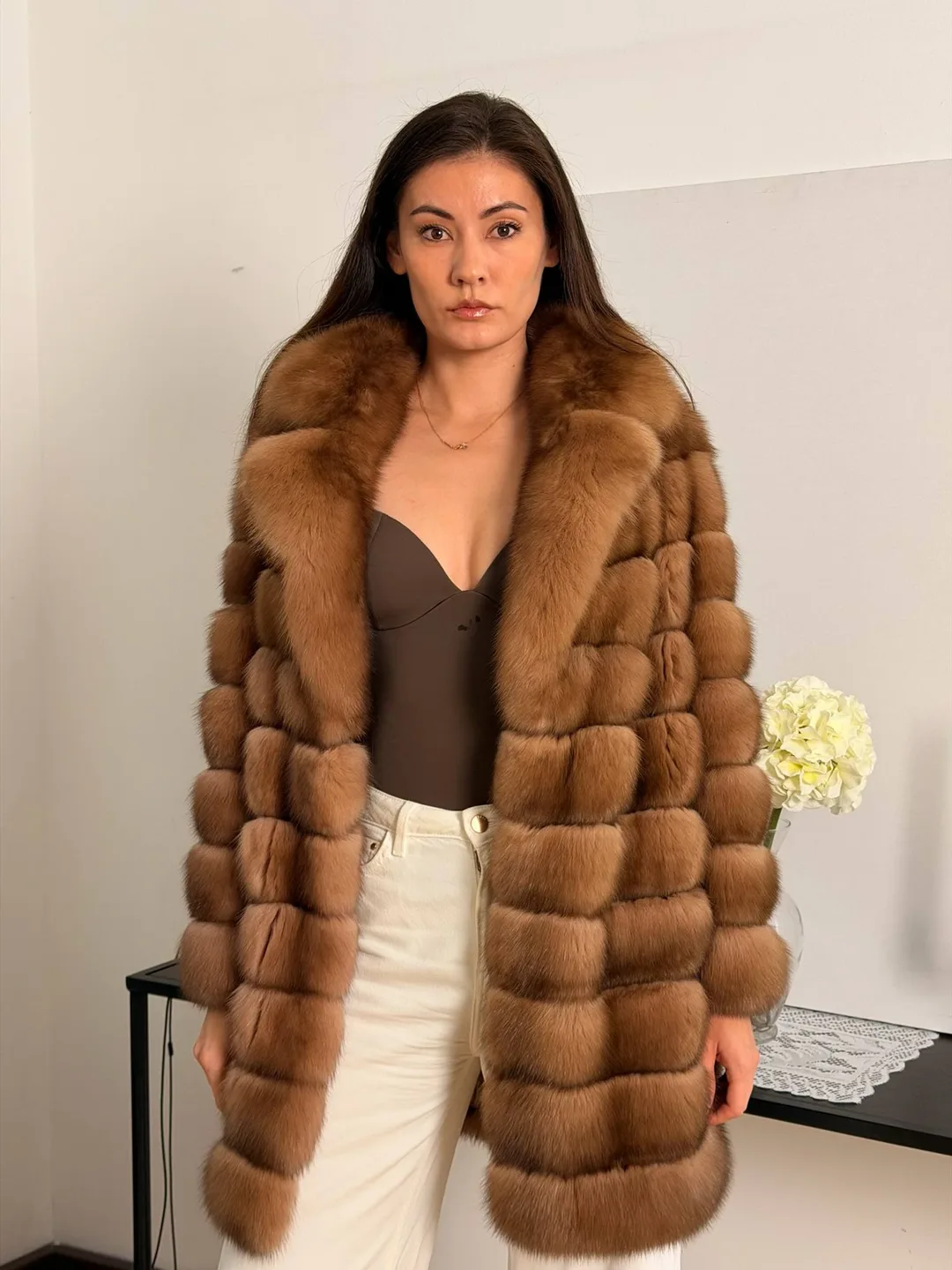 Modella di fronte in un cappotto di zibellino color miele con ampio collo, pantaloni avorio