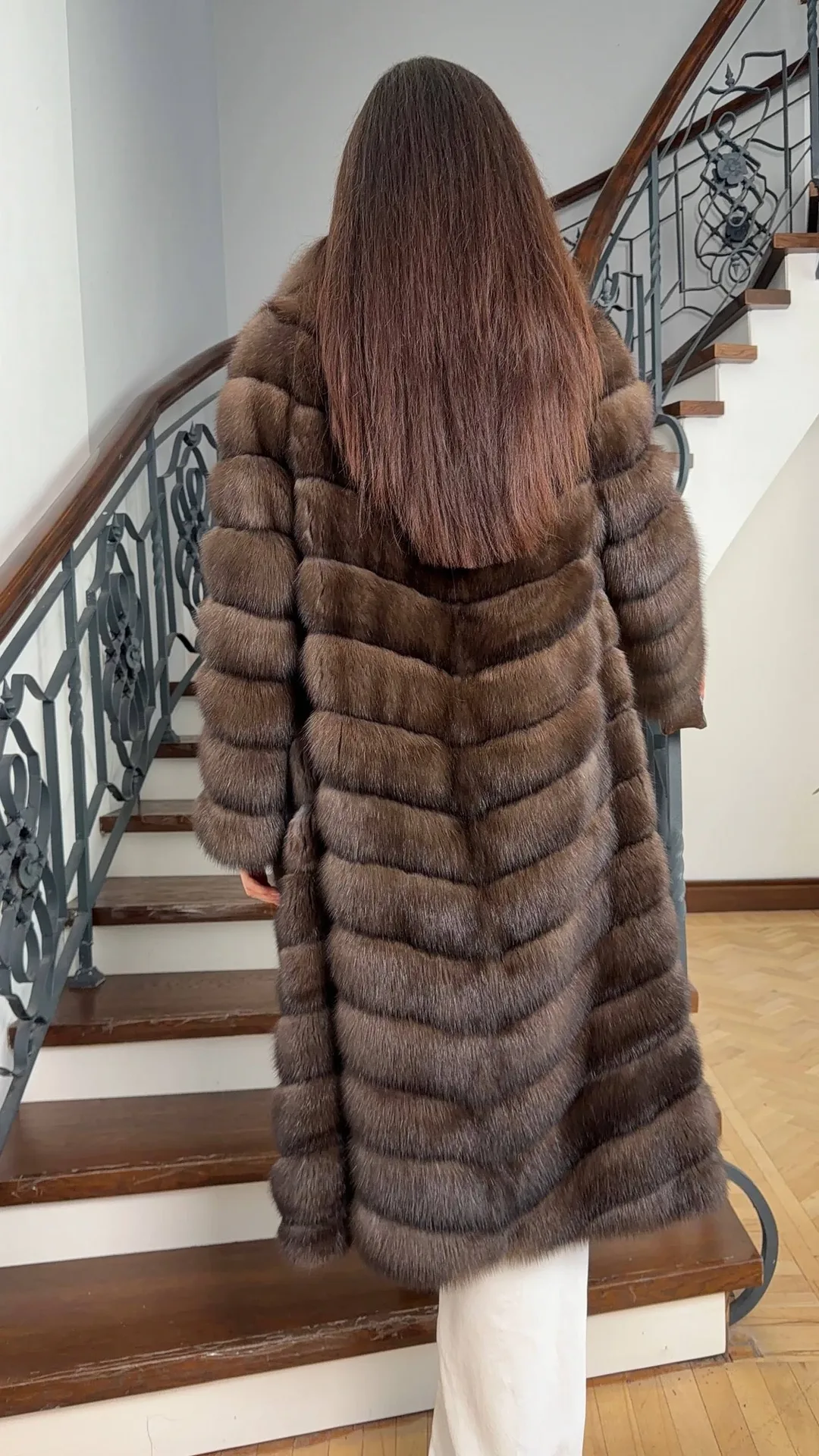 Modella di spalle su una scala in un cappotto lungo di zibellino